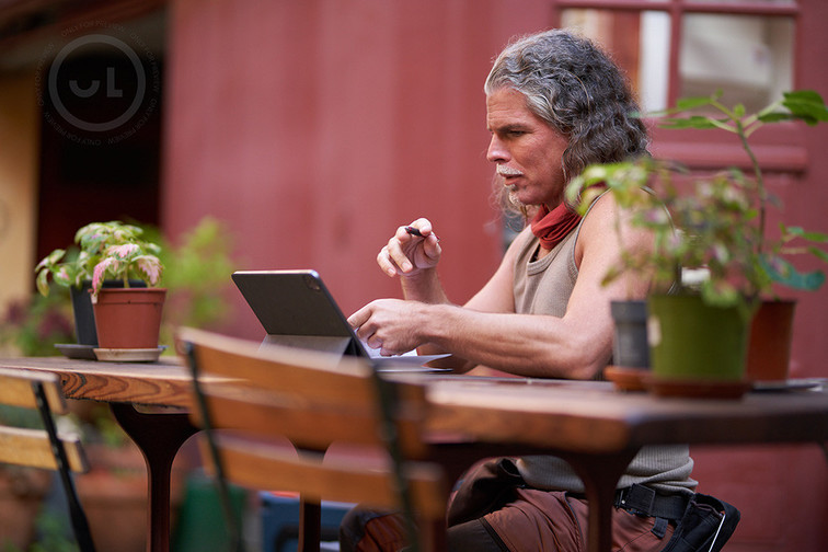 Man in a brown singlet sitting on a table outside looking at his laptop