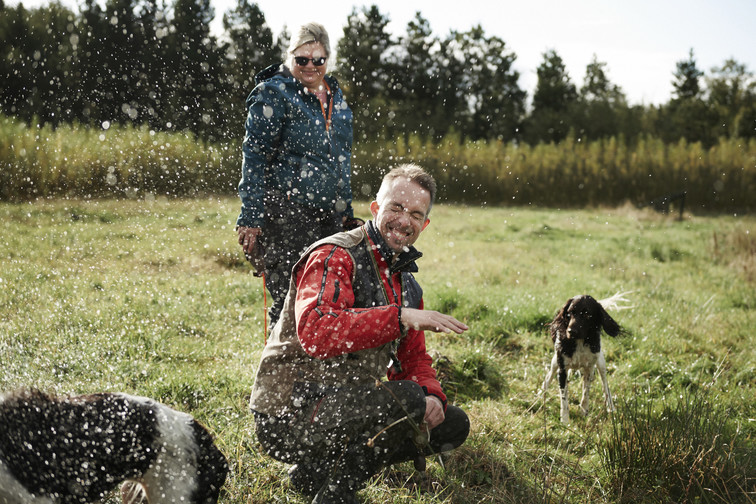 A man gets splashed by his dog shaking off water while in a field.
