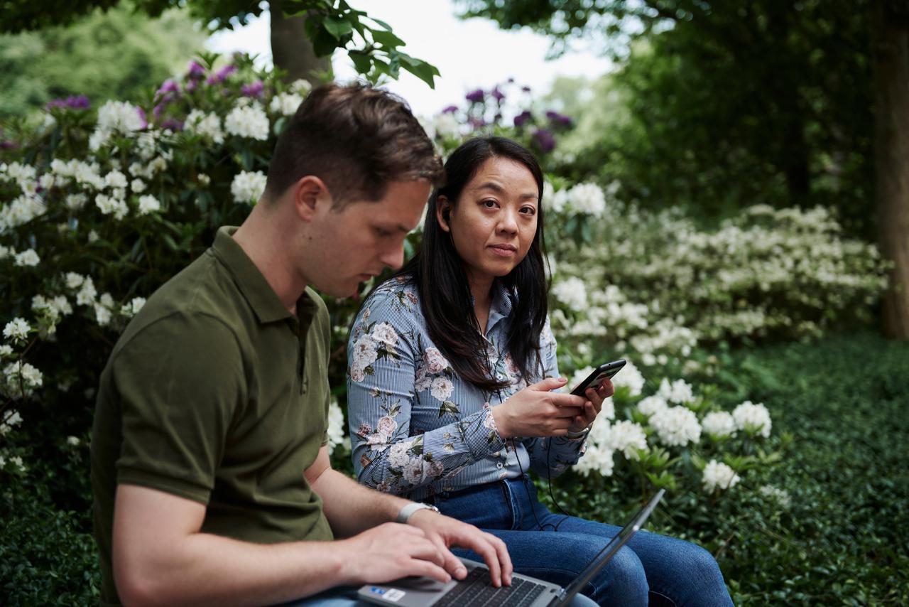 Man and woman sitting on bench, working on devices