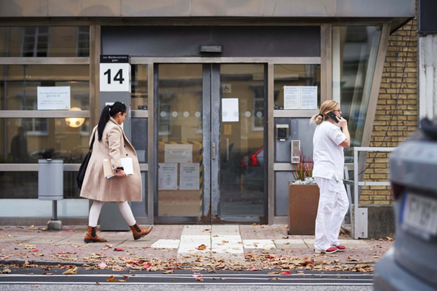 A woman walks into her office from the street as a nurse stands nearby talking on the phone.