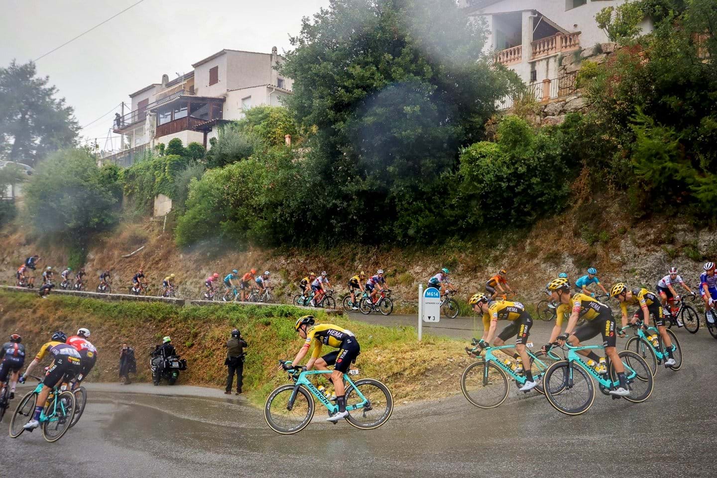 Cyclists go around a turn on a wet and rainy day at the 2020 Tour de France.