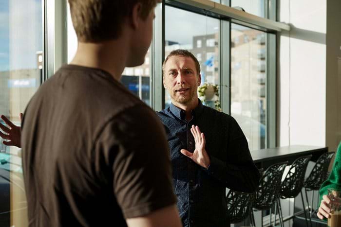 Two colleagues discuss something in front of an office window.