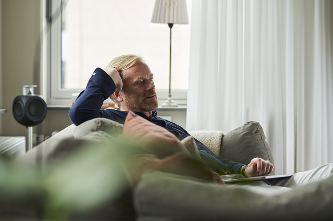 A blonde man in a blue collared shirt relaxes on the sofa at home