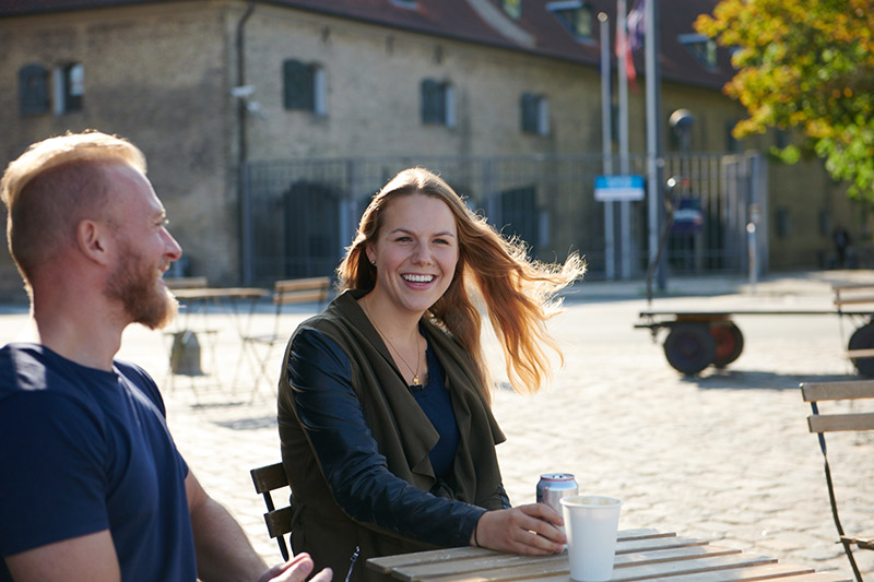 A women and man laugh while sitting at a small cafe table in the sun.
