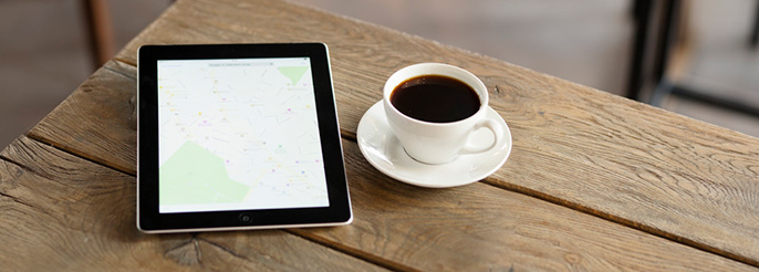 A table with a cup of coffee and an iPad showing a map.