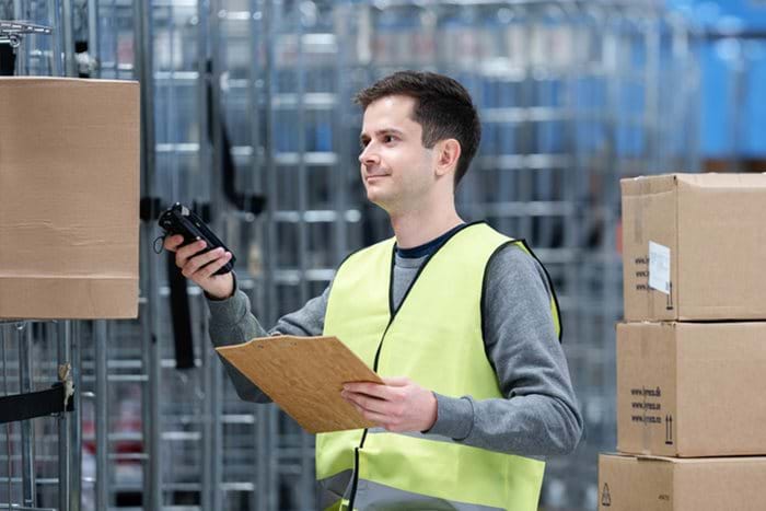 A warehouse worker scans a box while holding a clipboard.