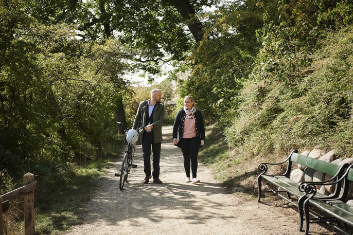 A woman and man colleague walk along a gravel road in a park during their lunch break.